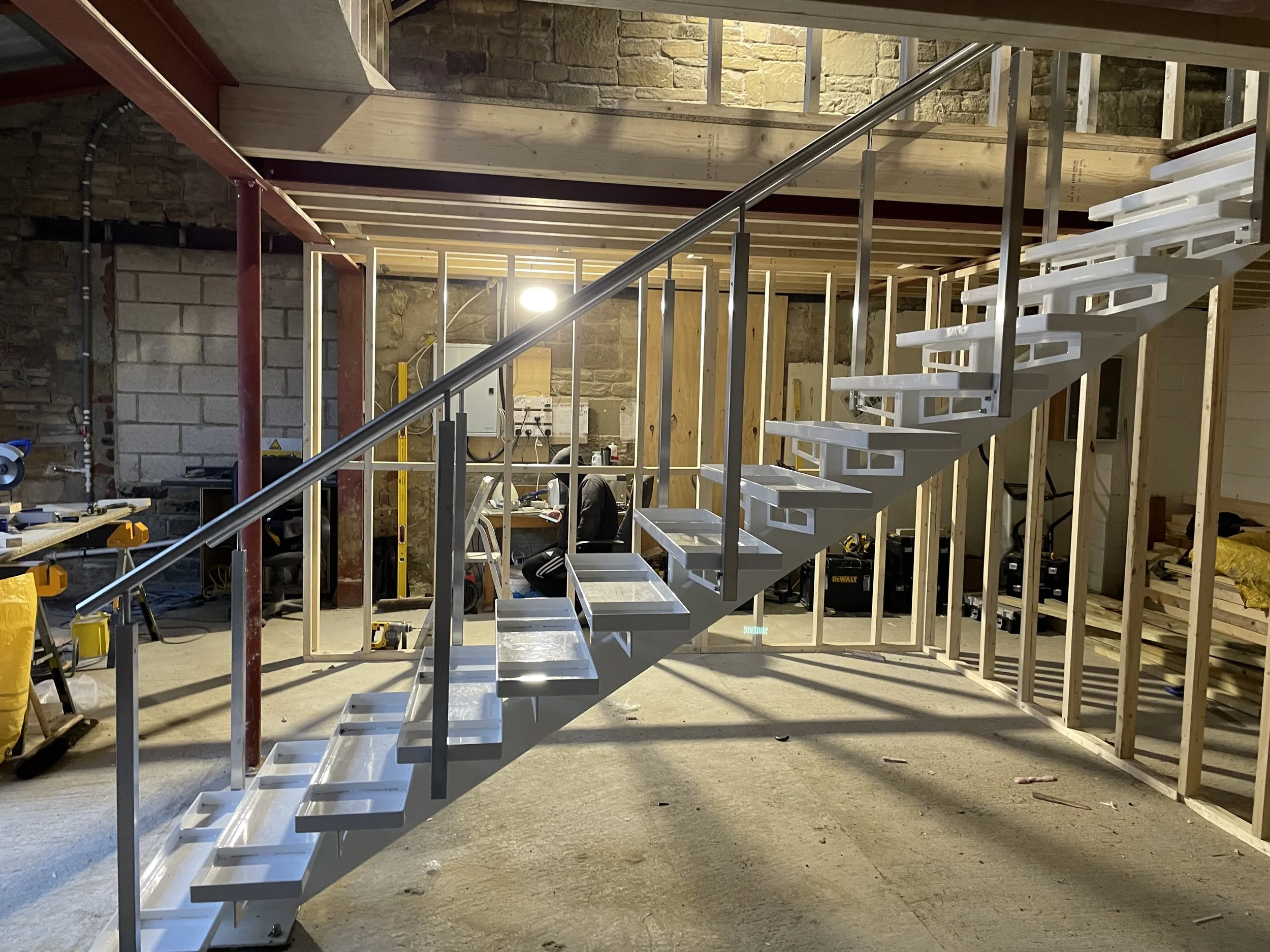 Bespoke steel staircase with an open tread framework and stainless handrail, shown during installation ahead of the finished treads being fitted.