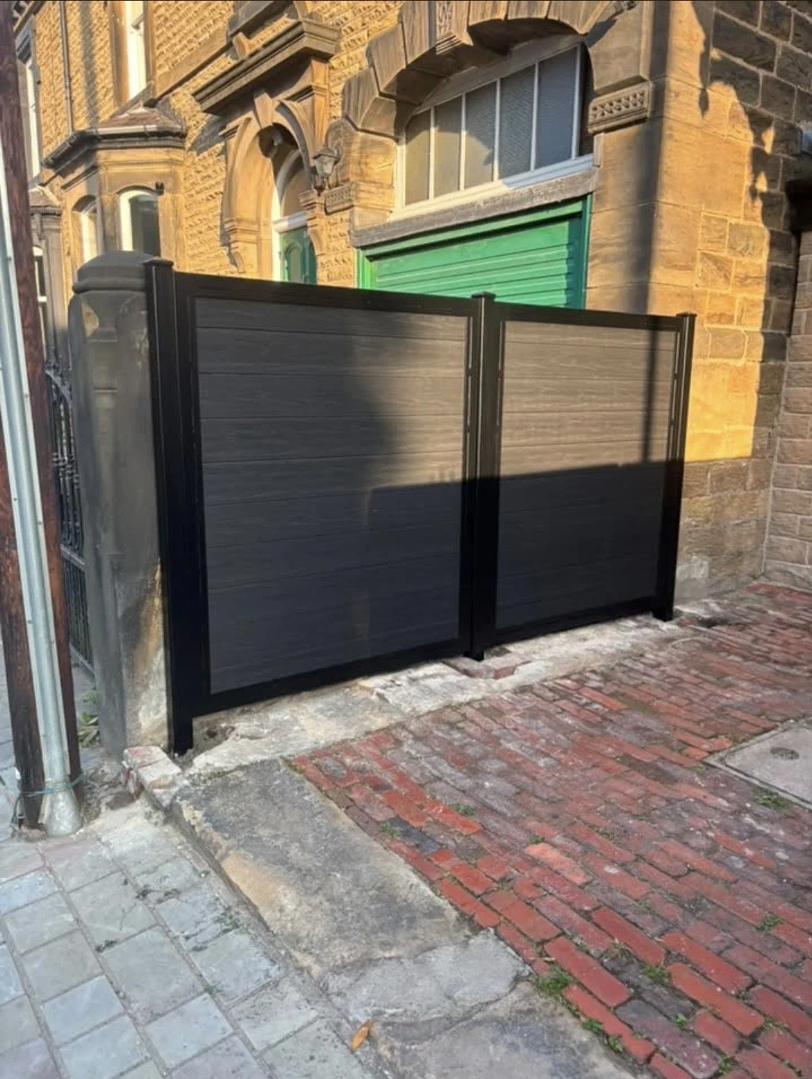 Bespoke black metal fence with horizontal composite infill panels, designed to provide privacy and security beside a traditional stone property.