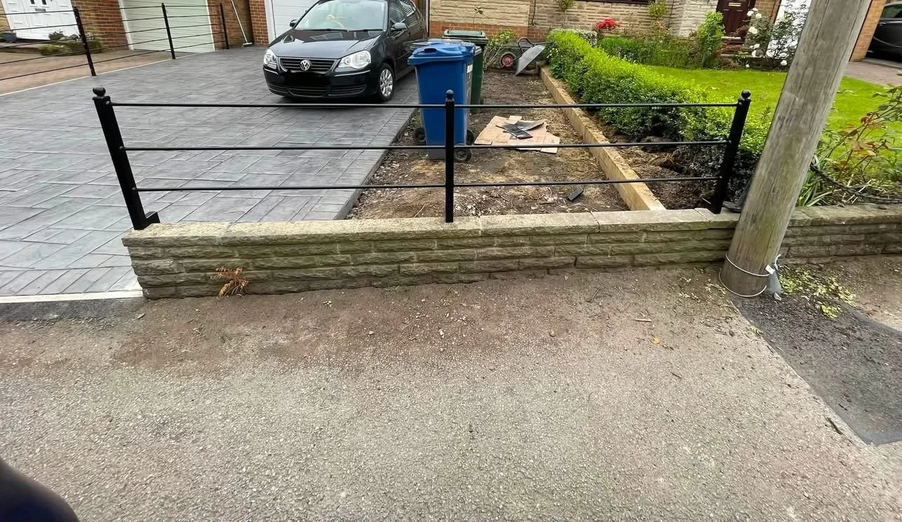 Black steel estate style railing with horizontal bars and decorative post tops, fitted above a low stone wall beside a driveway.