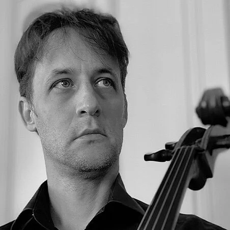 A man with dark hair looking upward while holding a cello.