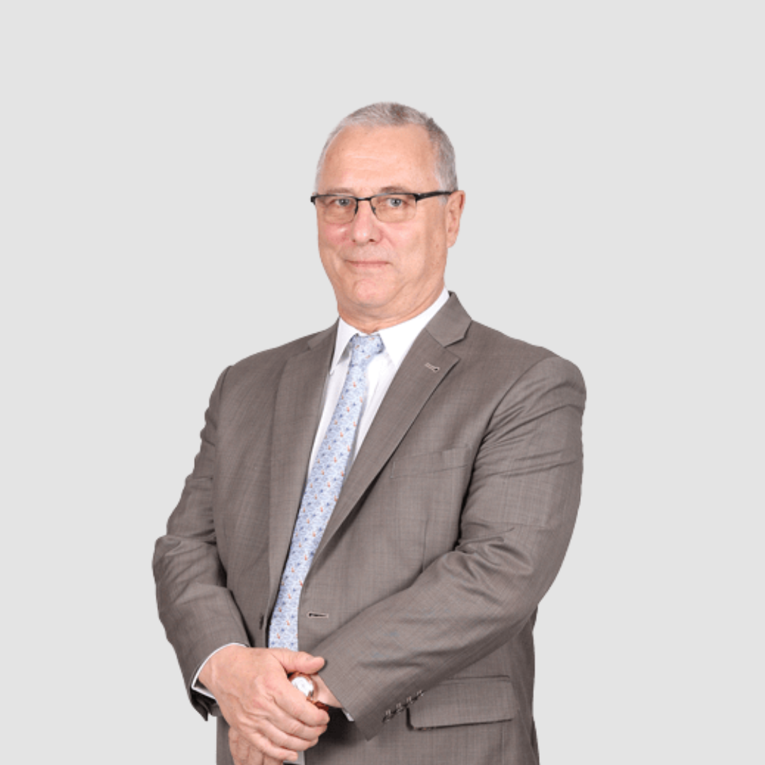 Portrait of a middle-aged man in a gray suit with glasses, standing with arms crossed against a light gray background.
