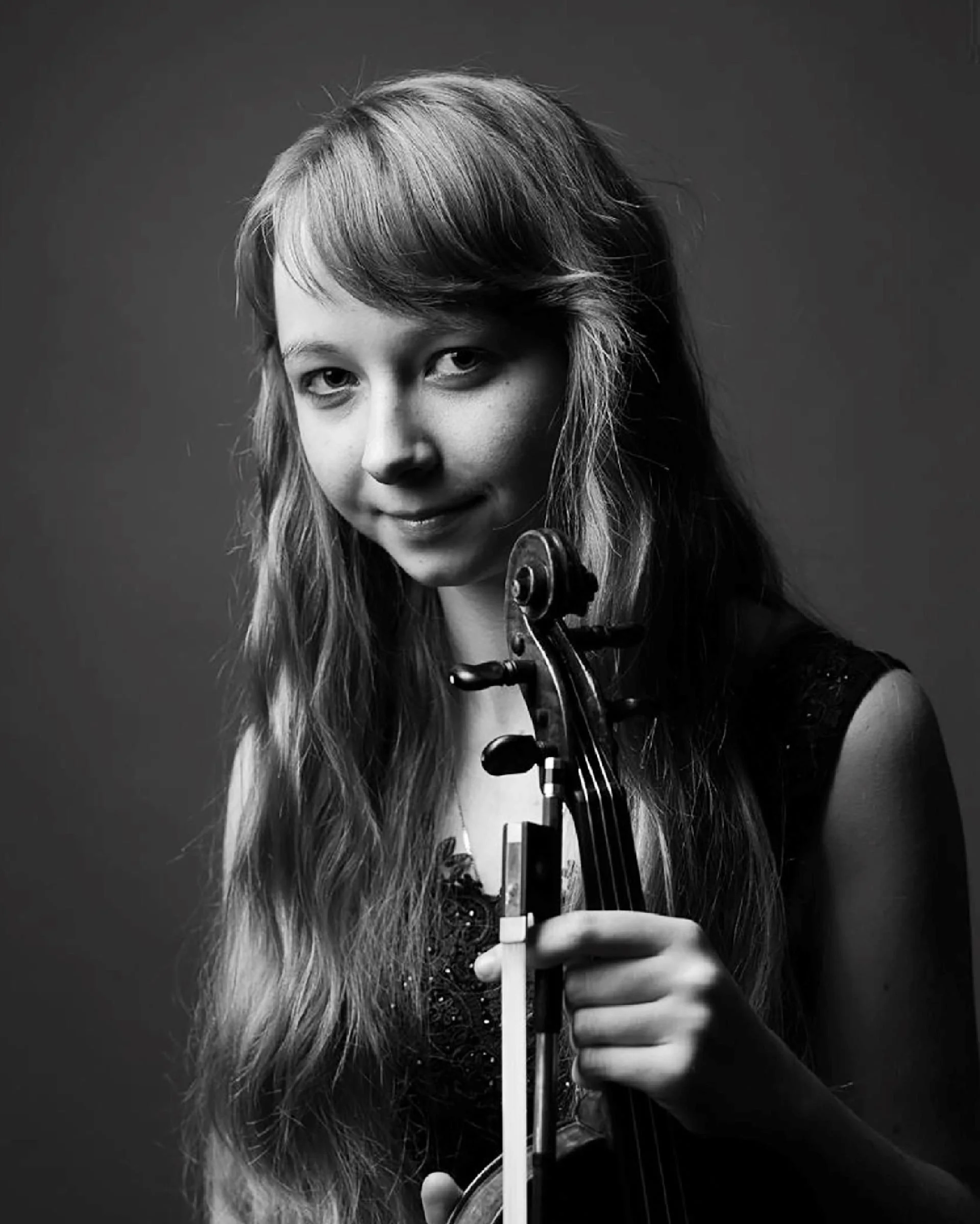 Black and white photo of a woman with long hair playing the violin, focused on her face and hand holding the bow.