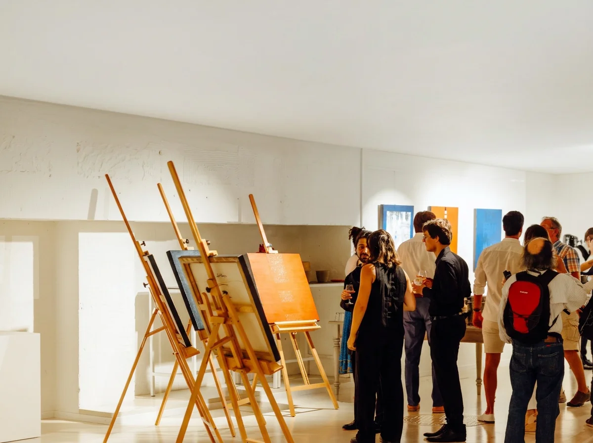 People attending an art gallery exhibition, viewing paintings on easels and wall.