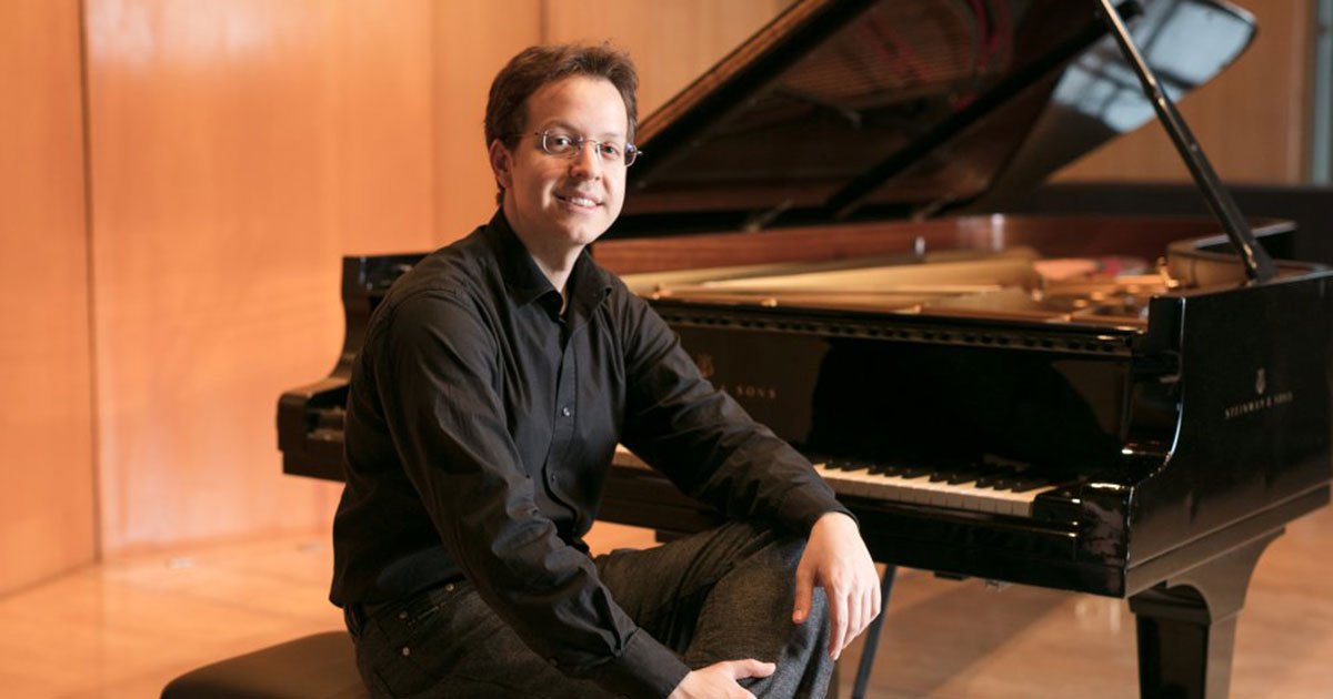 A man sitting on a bench next to a grand piano in a room with wooden walls
