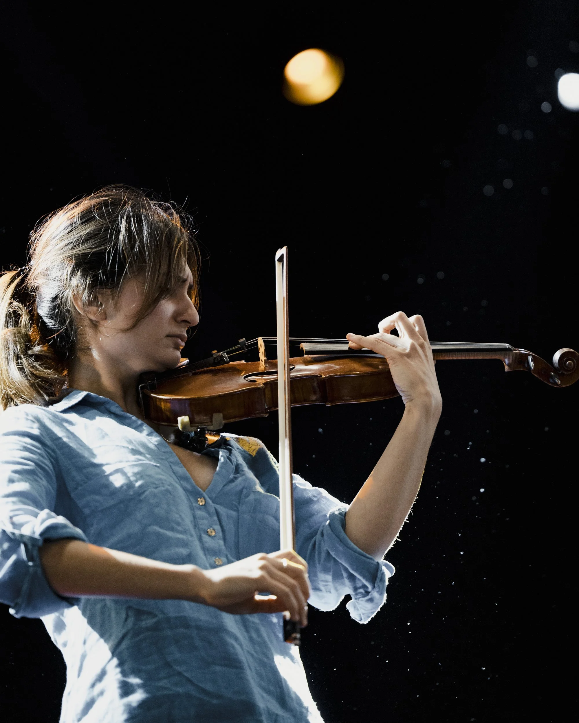 A woman with light brown hair plays the violin in space, with a dark starry background and a large yellow planet visible above her.