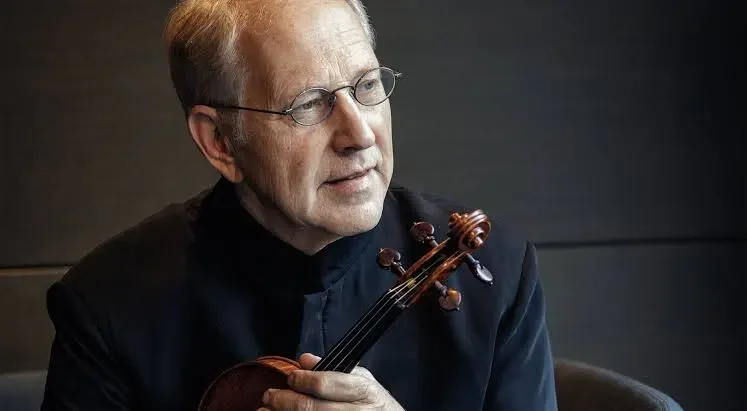 An elderly man with glasses holding a violin.