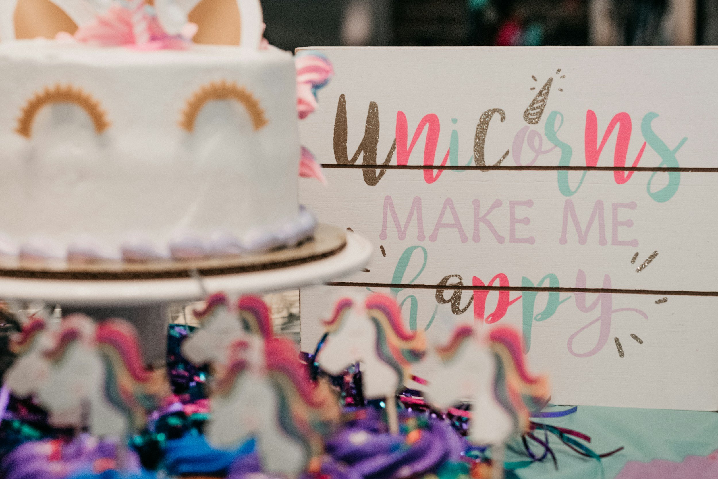 Colorful rainbow-themed birthday decoration with a cake and a sign reading 'Unicorns Make Me Happy.'