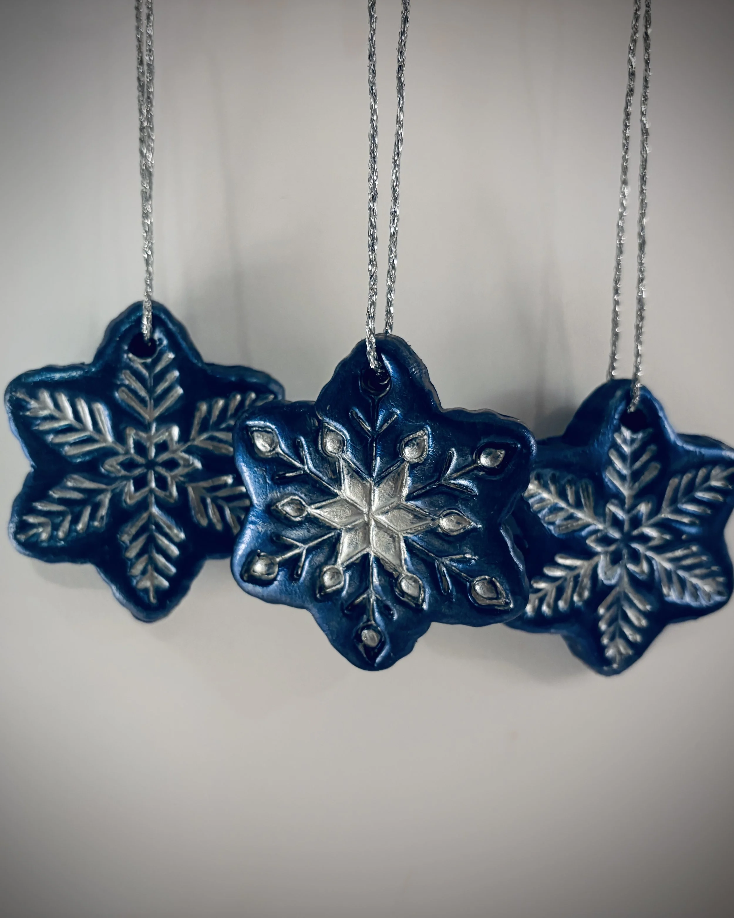Three blue and silver snowflake-shaped ornaments hanging from silver strings against a plain background.