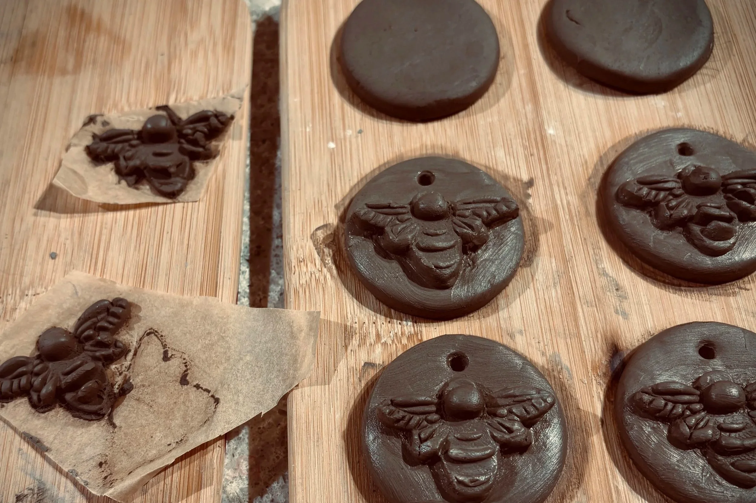 In progress wet-clay bee baubles, with detailed wing patterns on a wooden surface.