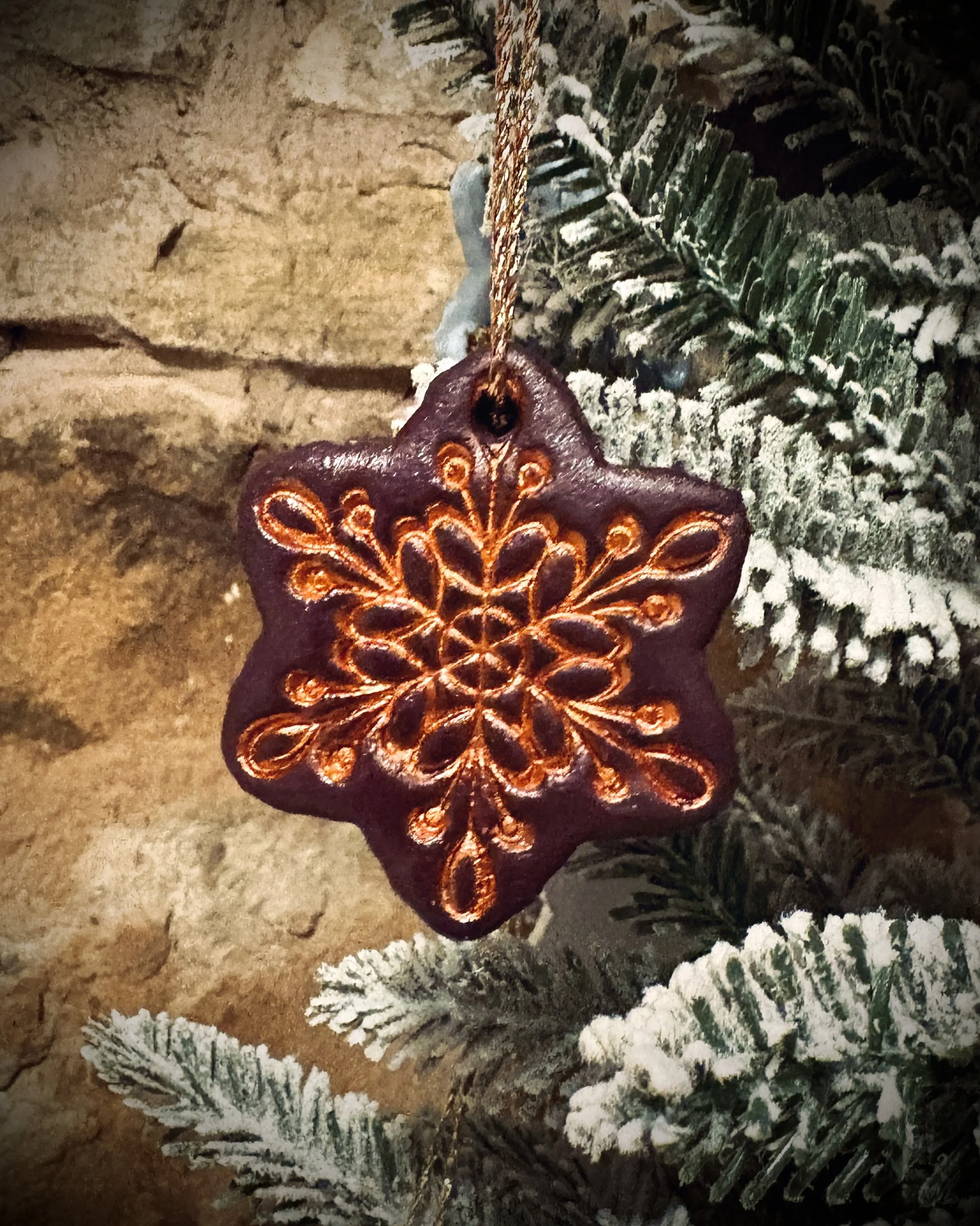 Decorative illuminated snowflake bauble hanging among snow-dusted evergreen branches and tree trunk.