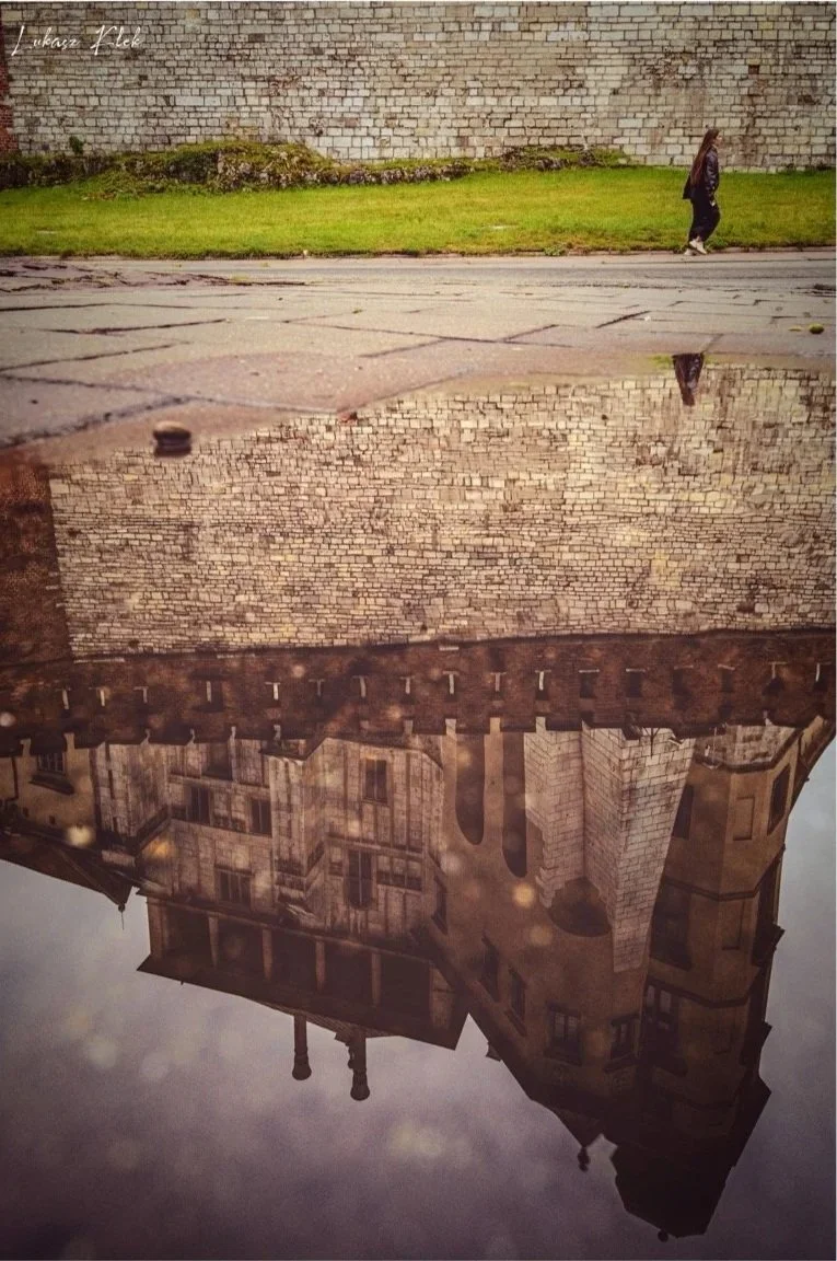 Reflection of a historic building with stone architecture in a puddle on the street.