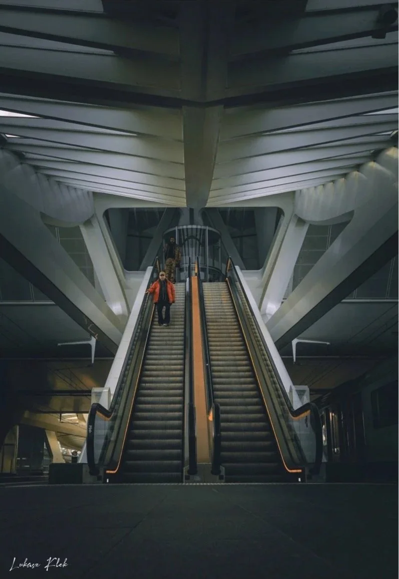 People riding on escalators inside a modern building with futuristic architecture.