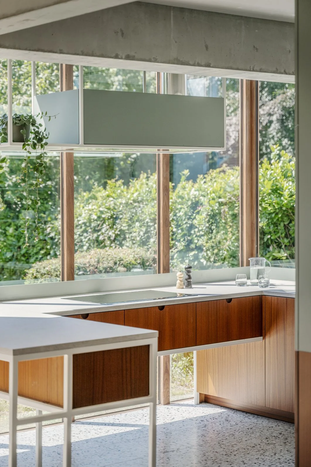 Een keuken met grote ramen, houten kasten, een wastafel, een waterkruik en glazen.