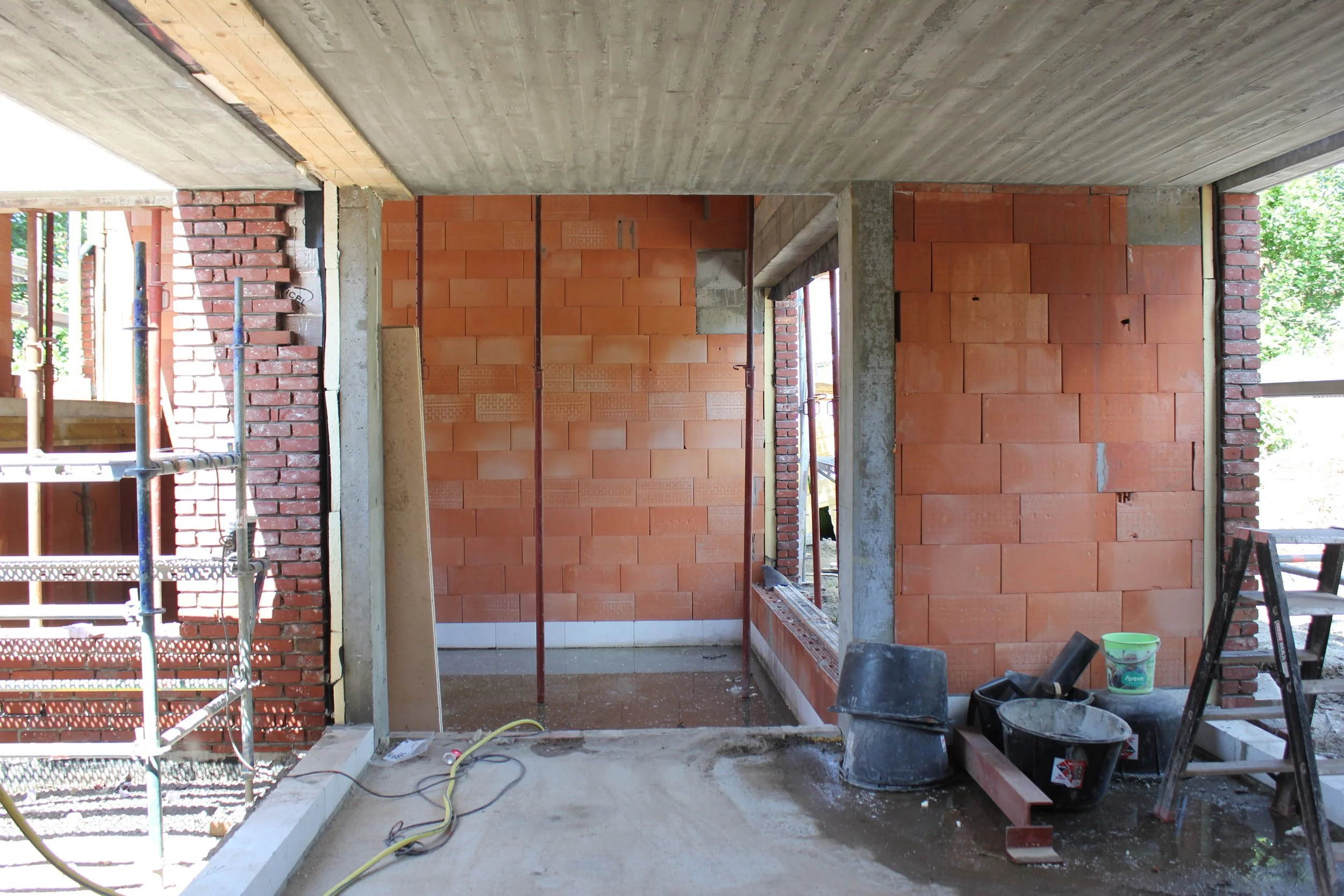 Binnenkant van een betonnen en bakstenen gebouw onder constructie, met bouwgereedschap en materialen op de vloer.