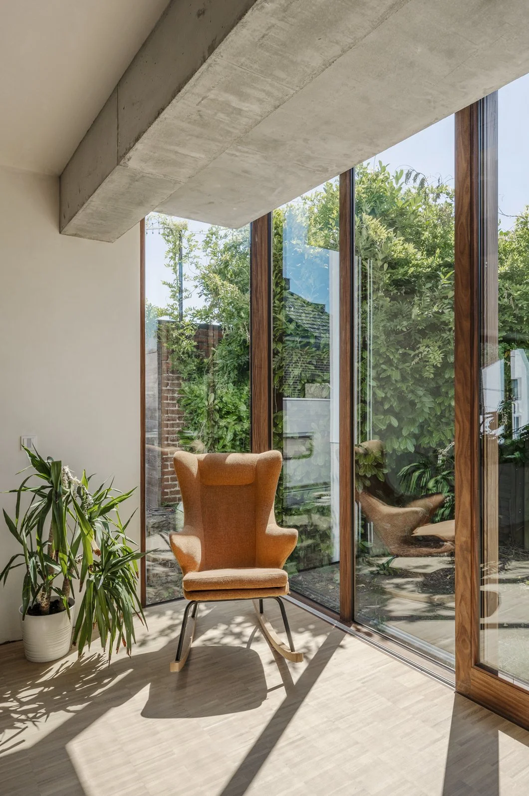 Een modern interieur met een rotan armstoel, een grote glazen deur en veel groen buiten.