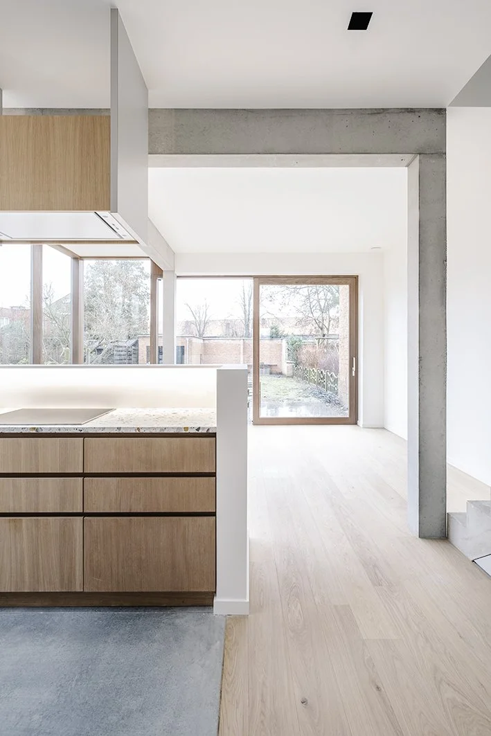 Interieur van een modern huis met grote ramen, houten kasten, een betonnen muur en lichte houten vloeren.