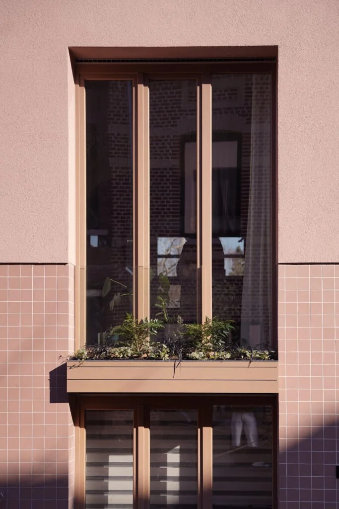 Raam met plantenbak op de buitenmuur van een gebouw met een zandkleurige gevel en rookkleurige omlijsting.