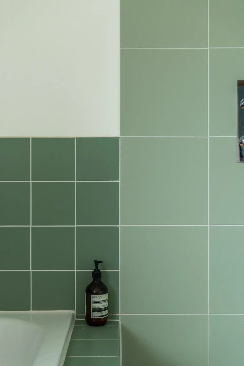 Groene betegelde muur met een zeeppompje en een witte badkuip in de badkamer.