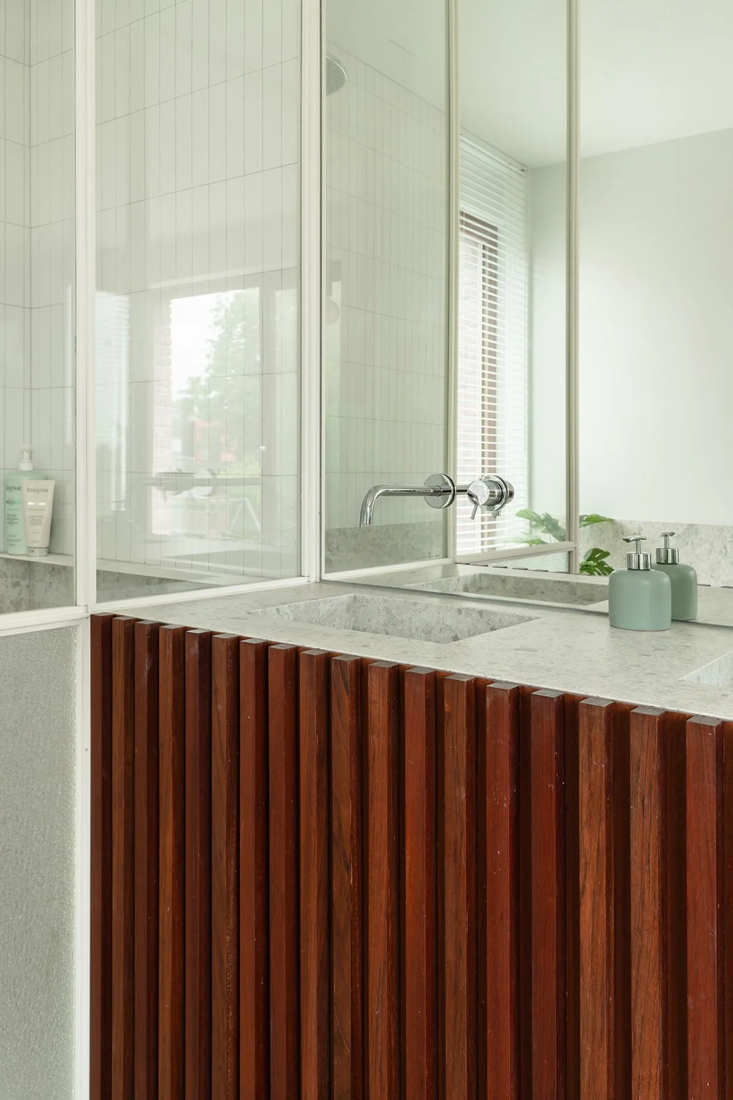 Een badkamer met een dubbele wastafel met een granietenblad, een spiegel, twee zeepdispensers en een plafond met raamluiken.