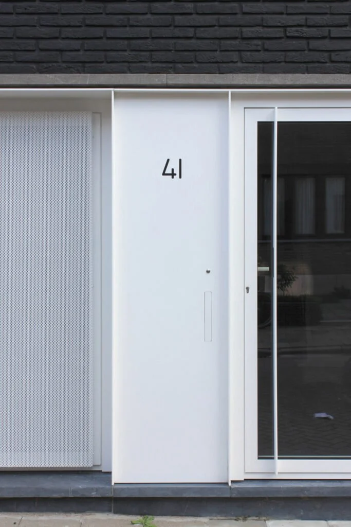 De gevel van een modern gebouw met een witte deur en een deur met een grote glazen schuifdeur, genummerd 41.
