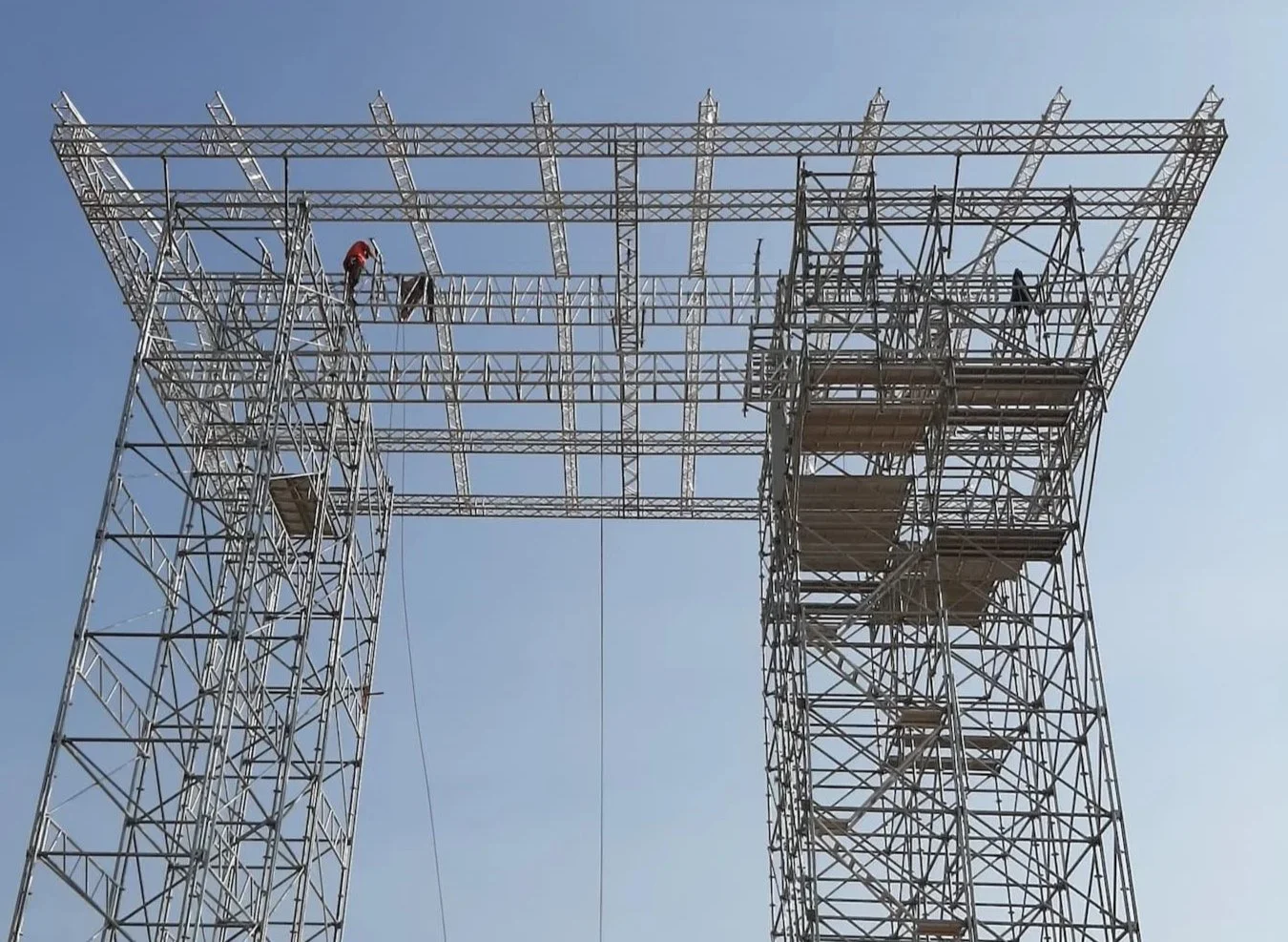 Rope-Access construction workers building a tall metal scaffold structure against a clear blue sky.