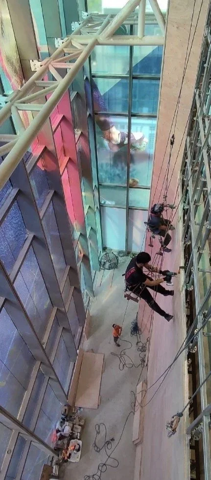 Rope-access workers installing climbing panels onto a high roped wall.