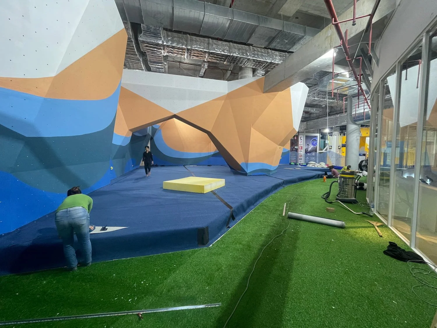 Indoor climbing wall under construction, green artificial turf, fall protection matts and climbing wall finished textured coating.