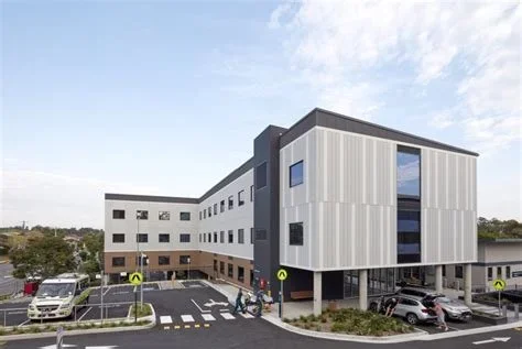Modern multi-story hospital building with parking lot and pedestrian crossing