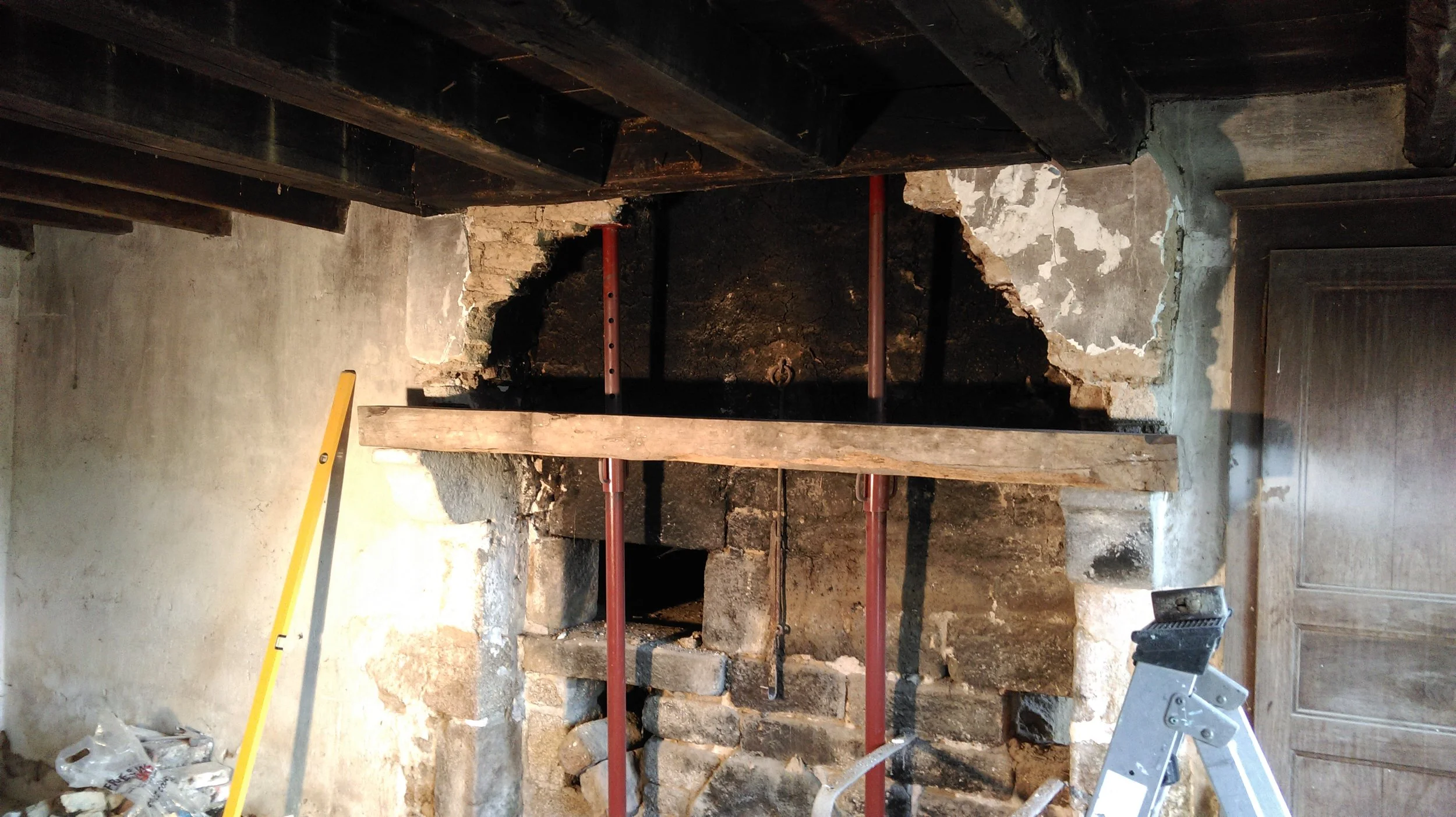french farmhouse undergoing chimney renovation with a large hole in the wall, construction tools, a yellow level, and scaffolding.