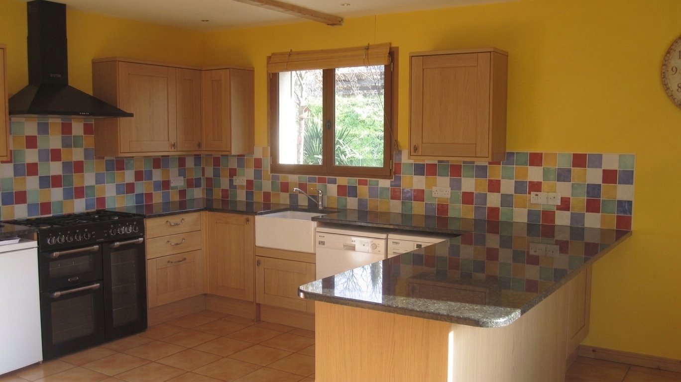 Kitchen with wooden cabinets, colorful tile backsplash, yellow walls, black stove, is also a dishwasher, window above sink, and a clock on the yellow wall.