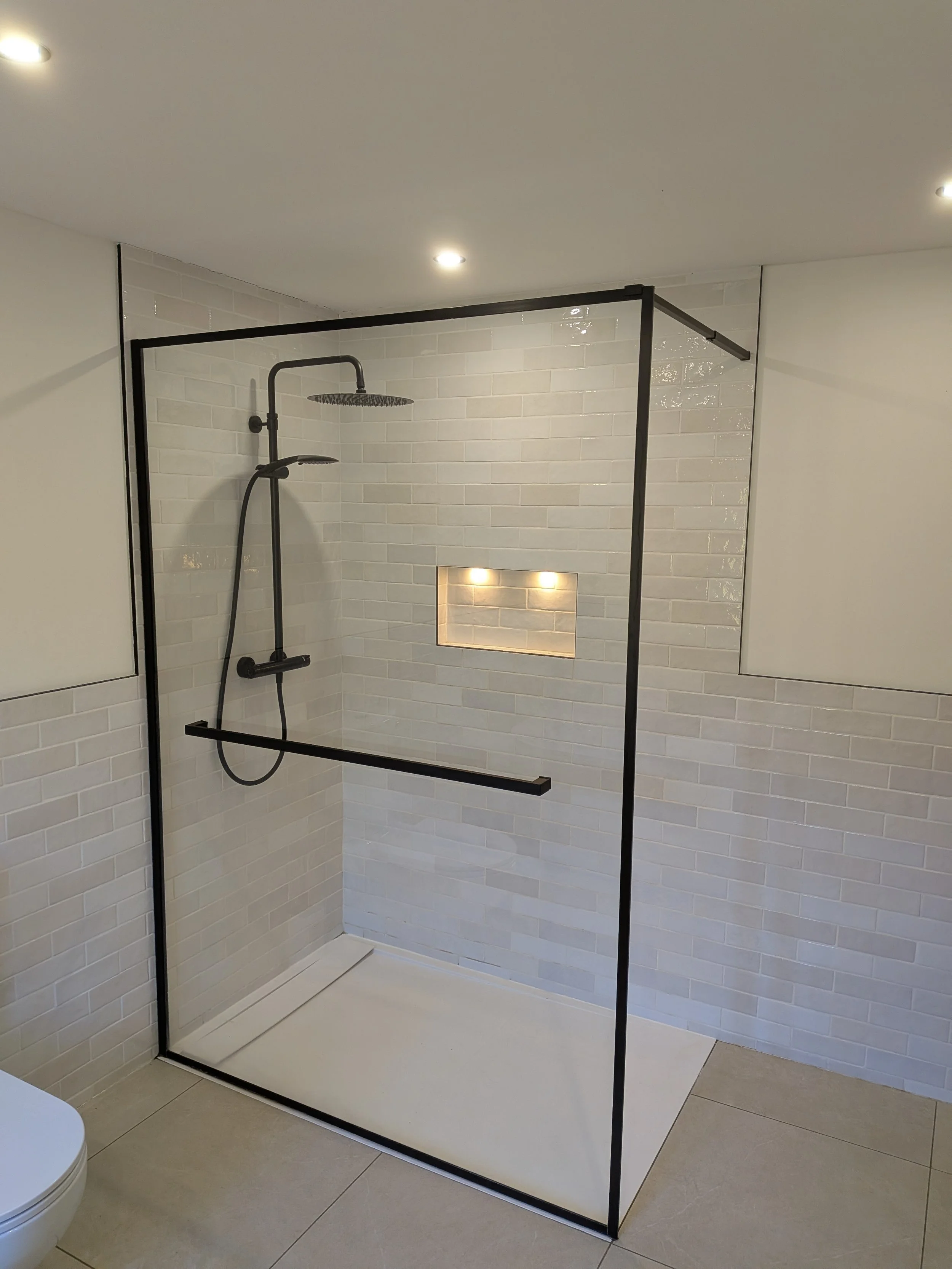 Bathroom shower with black metal frame, white brick wall tiles, built-in wall niche with lighting, ceiling-mounted rain showerhead, and handheld shower.