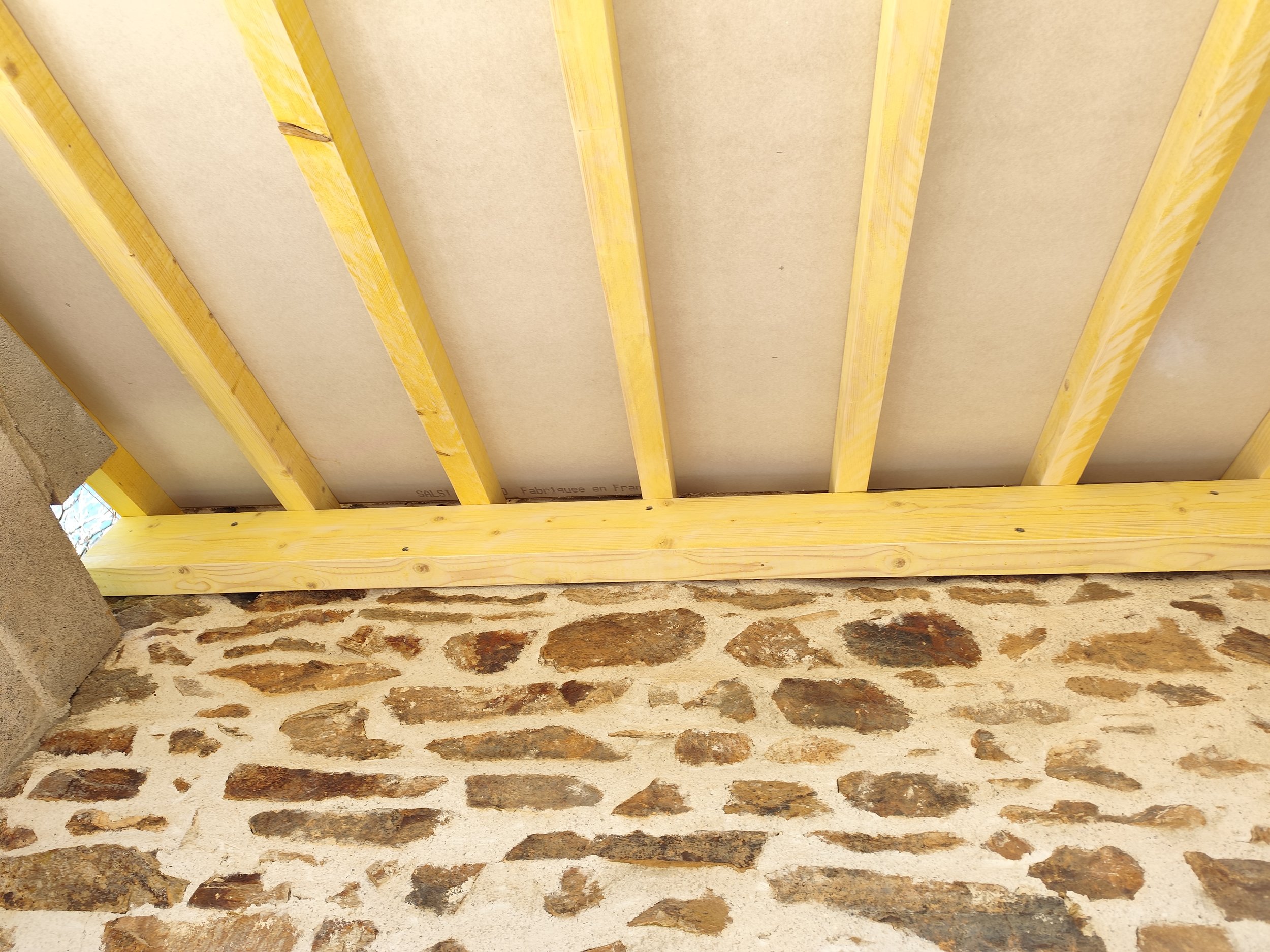 Ceiling with wooden beams and drywall, and a brick wall below.