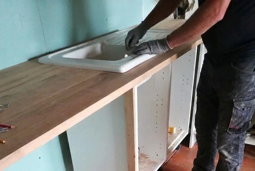 Person installing or repairing a kitchen sink on a wooden countertop.