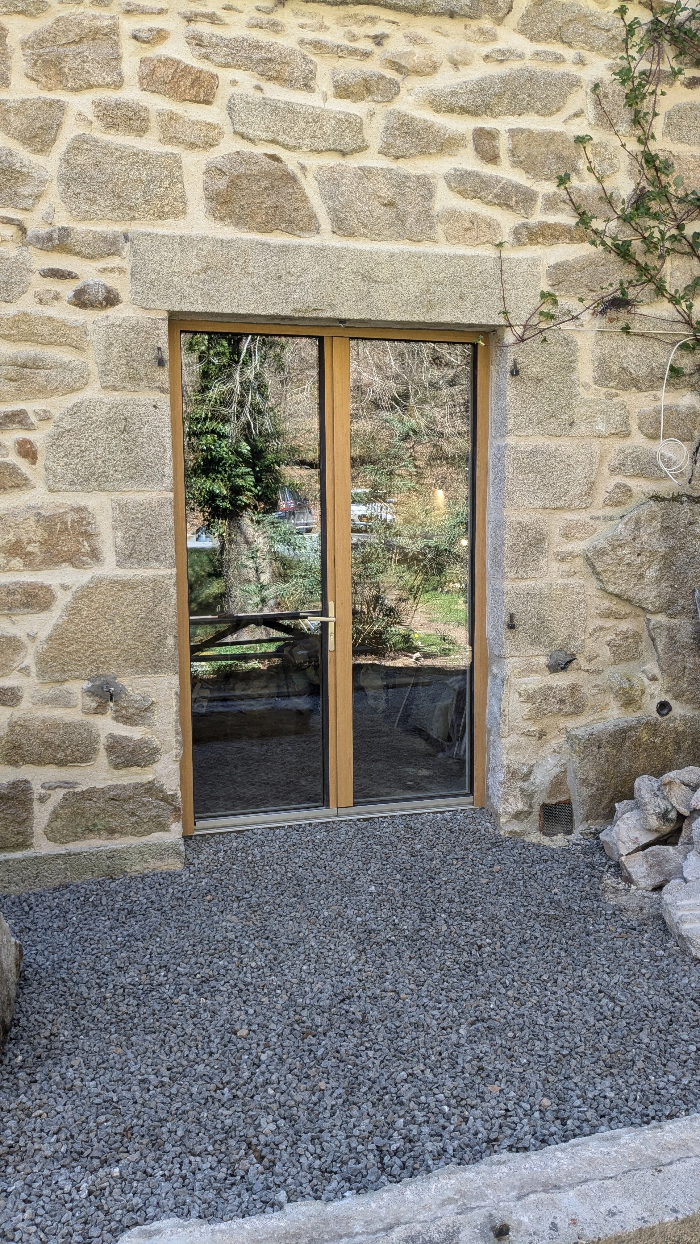 A stone wall with a wooden-framed glass door. Outside, trees and a parking lot are visible through the door's glass.