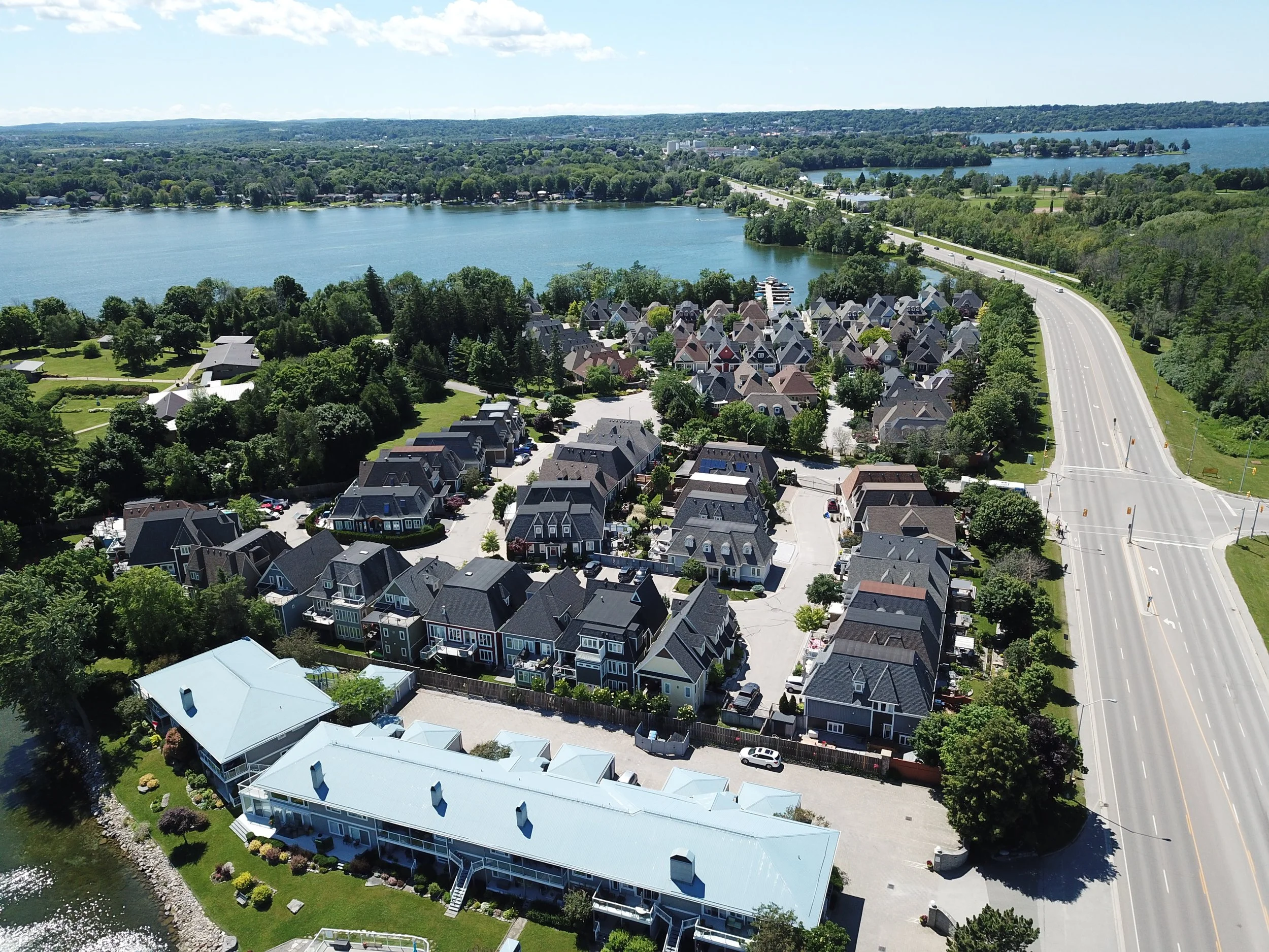 Aerial view of a lakeside residential neighborhood with houses, trees, a road, and a large body of water.