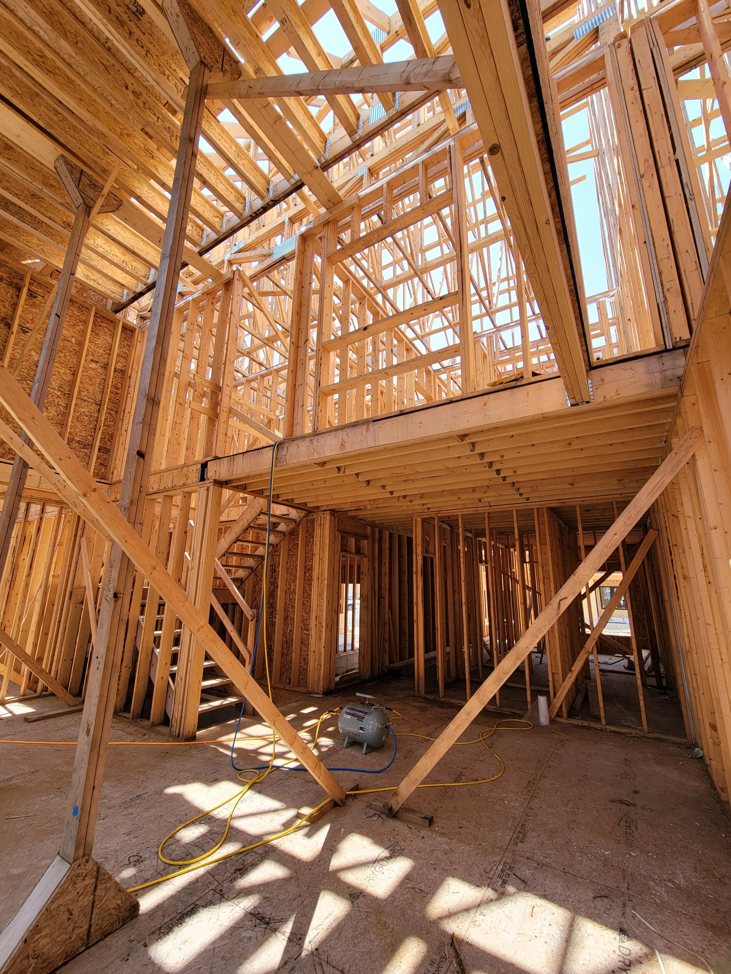 Interior view of a house under construction showing exposed wooden framing, scaffolding, and construction tools on the unfinished floor.