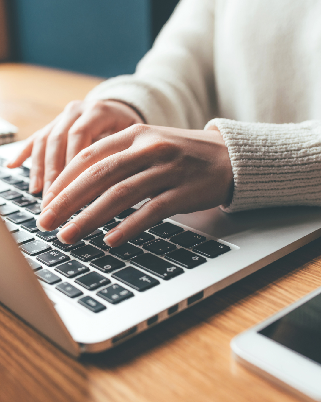Close-up of person's hands typing on a laptop keyboard on a wooden desk.