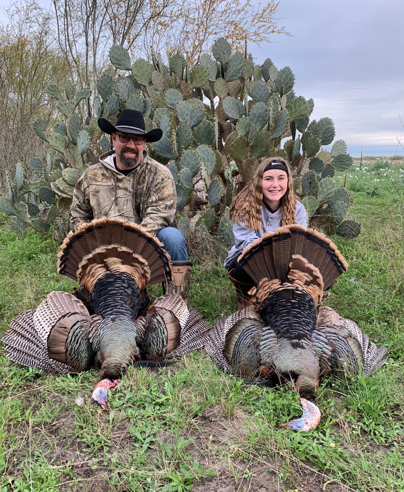 A man and a young girl with a cactus and a large turkey in a rural outdoor setting.