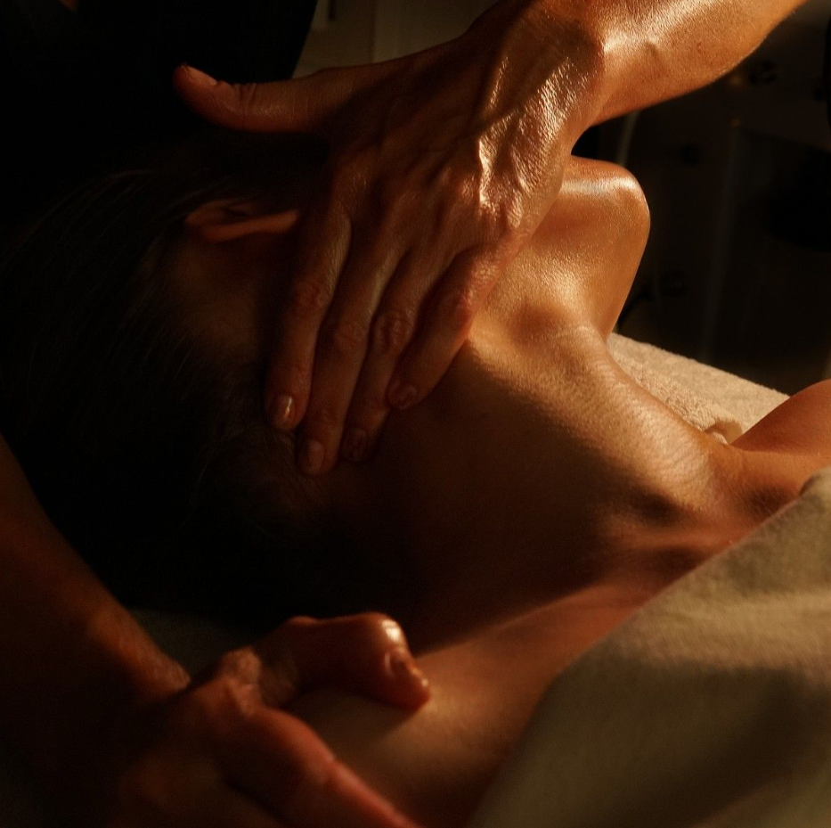 Close-up of a person receiving a massage, with hands applying pressure to their neck and shoulder area.