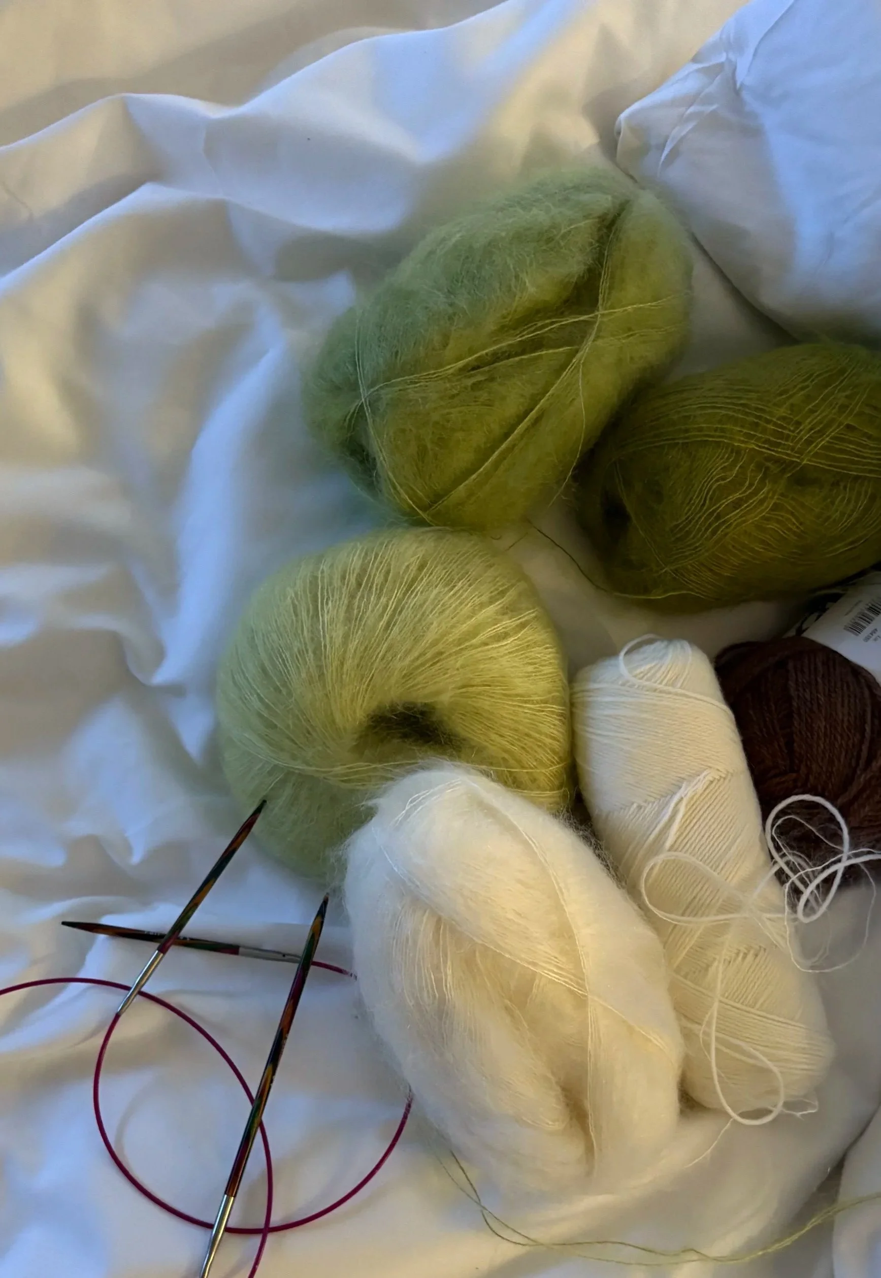 Haufen aus grünen und braunen Wollknäueln Mohair und Alpaca und Stricknadeln