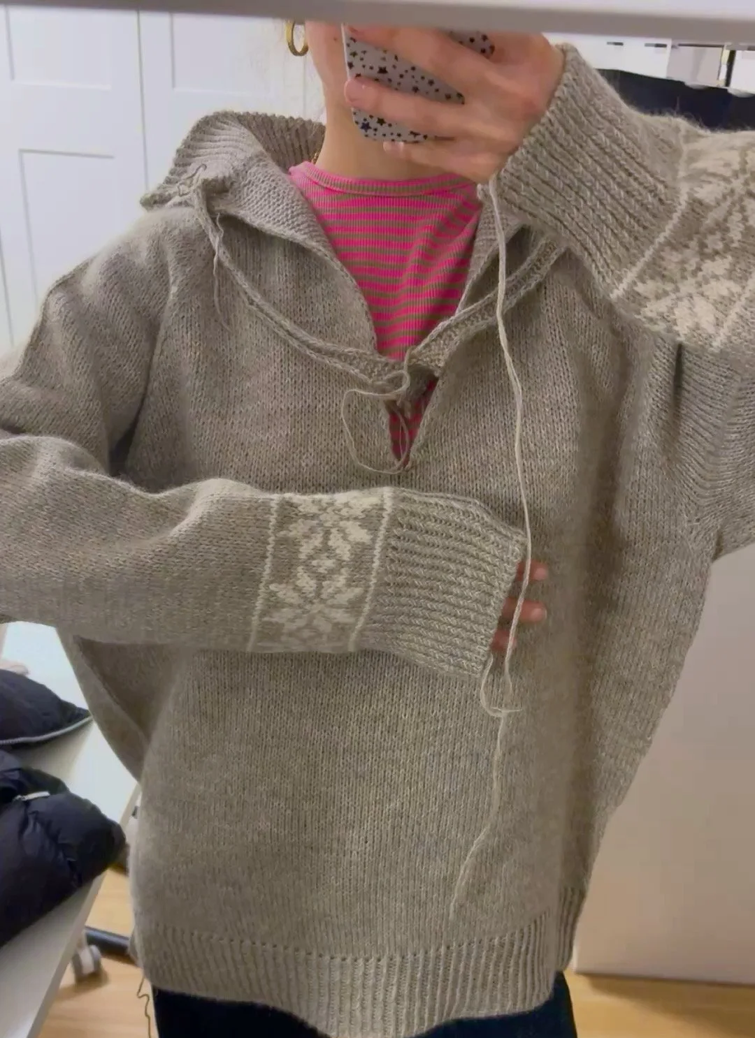 Person macht ein Spiegelbildfoto im Spiegel, trägt einen selbstgestickten Fair-Isle-Pullover in Grau mit Weißen Sternen und unfertigem Reisverschluss 
