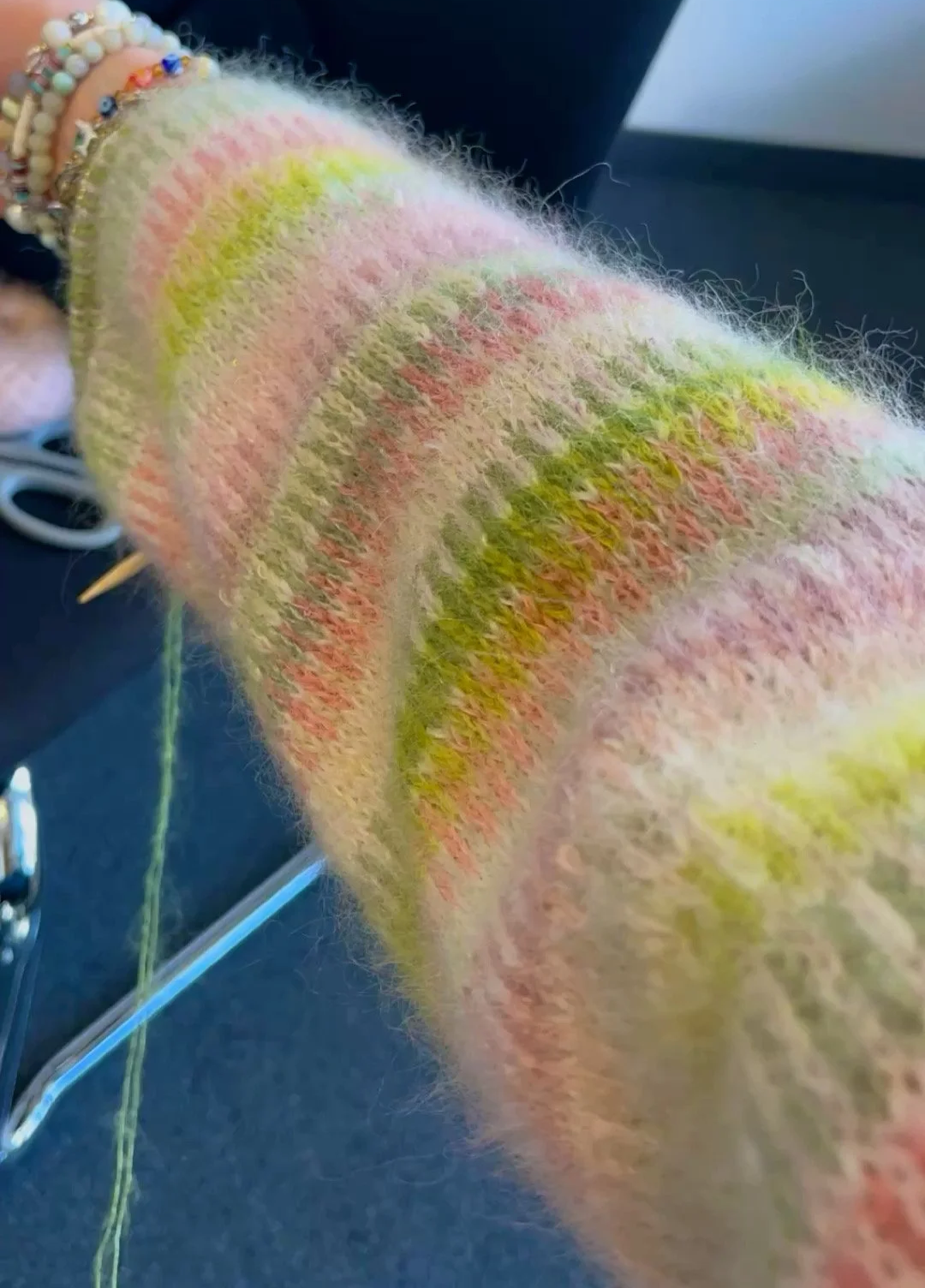Nahaufnahme eines gleichmäßig gestrickten, Fair-Isle-Muster Ärmel in Arbeit, MIt Rosa- und Grüntönen in streifenoptik.