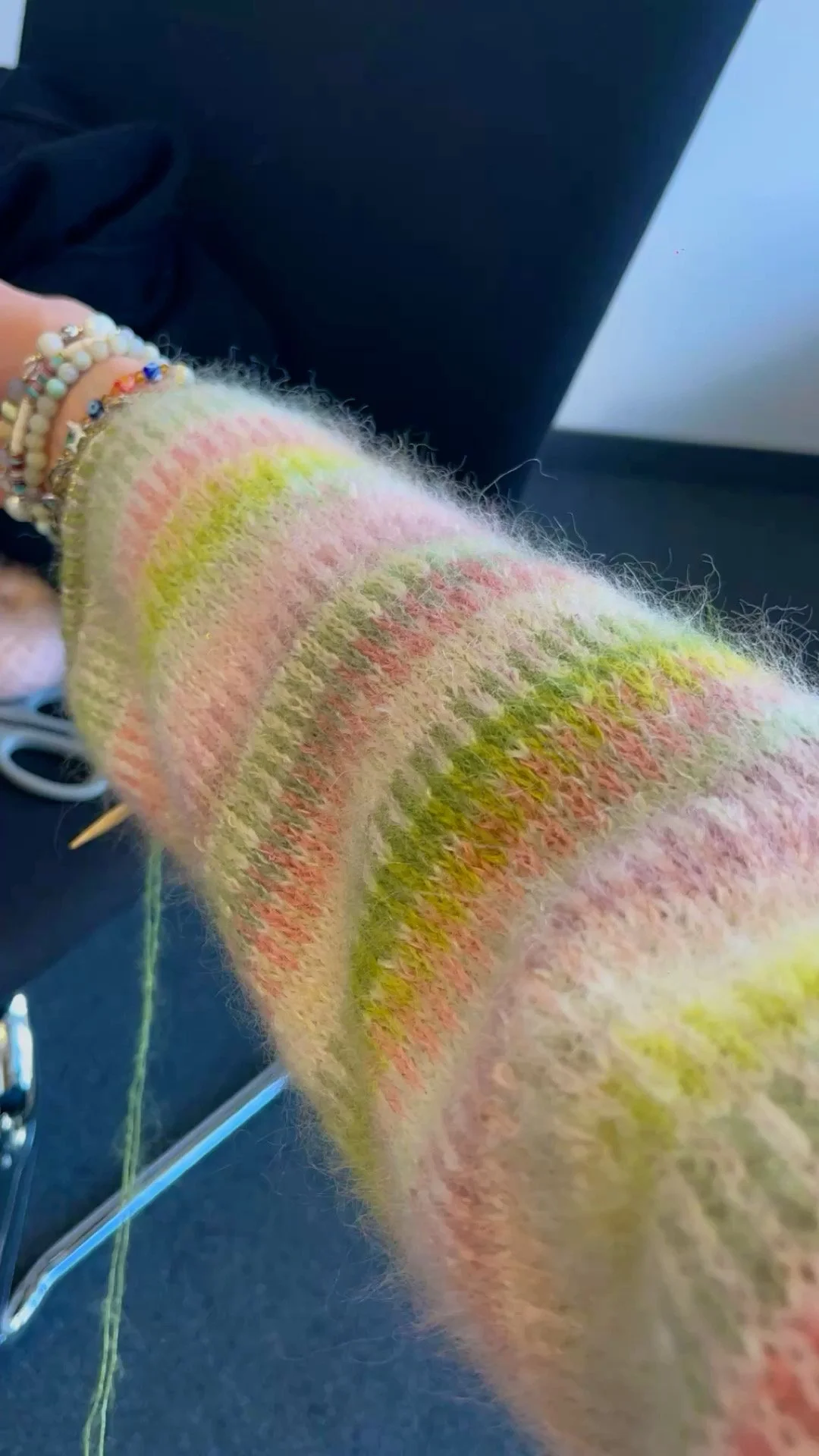 Nahaufnahme eines gleichmäßig gestrickten, Fair-Isle-Muster Ärmel in Arbeit, MIt Rosa- und Grüntönen in streifenoptik. 