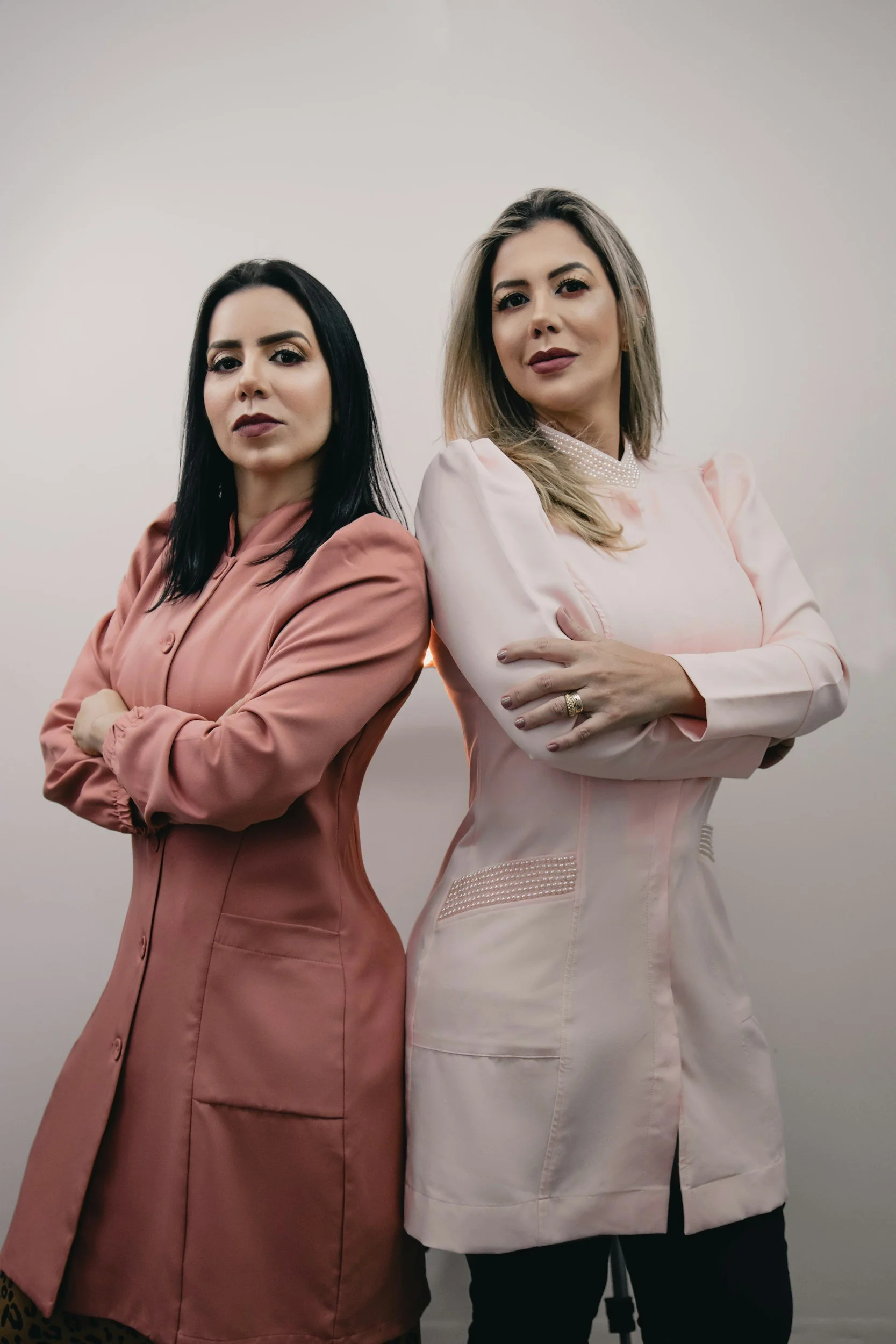 Two women standing next to each other with arms crossed, facing the camera, in front of a plain white background.