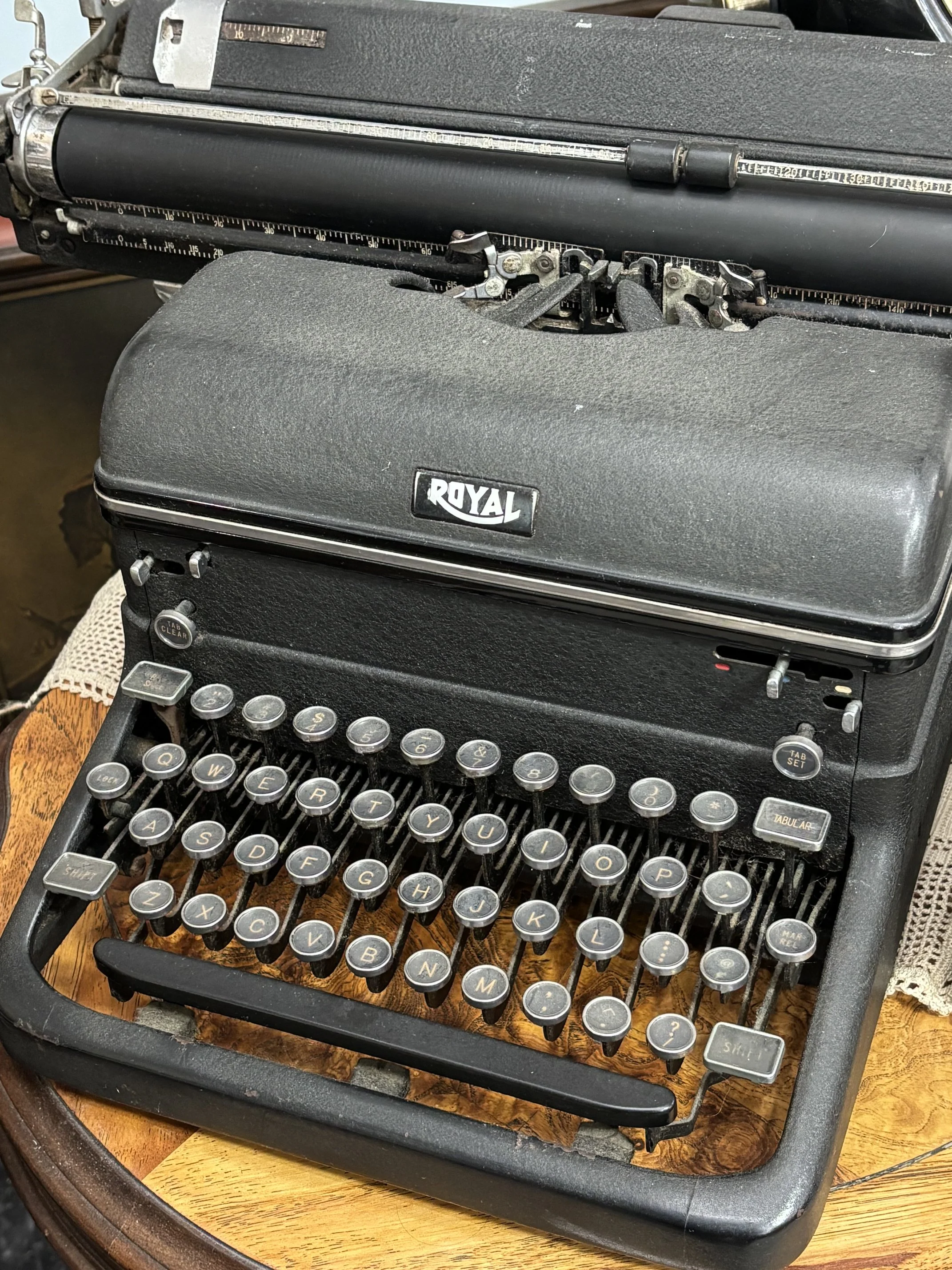 An antique Royal typewriter with round keys and a woodgrain base, placed on a wooden table.