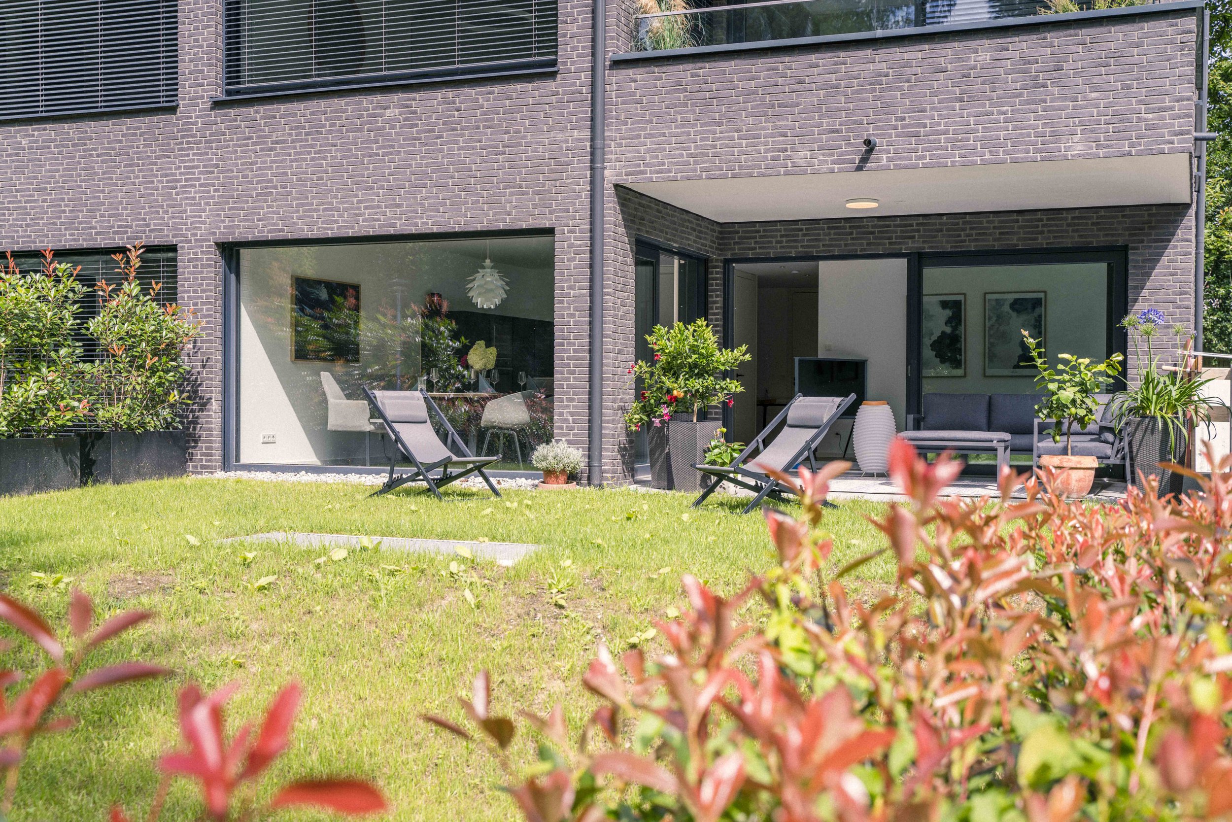 Modernes Mehrfamilienhaus mit Balkon, Terrasse und Garten, im Vordergrund bunte Blumen und grüner Rasen.