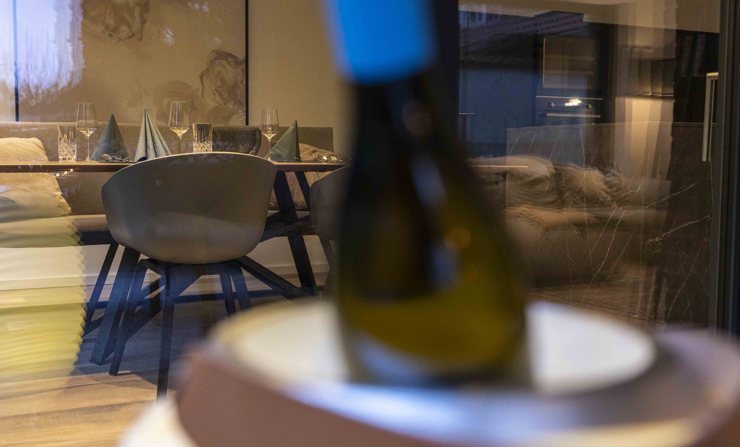Blick in ein elegant gedecktes Esszimmer mit Weingläsern, Besteck und Stoffservietten auf dem Tisch, durch eine Glasscheibe fotografiert, in einem modernen Restaurant.