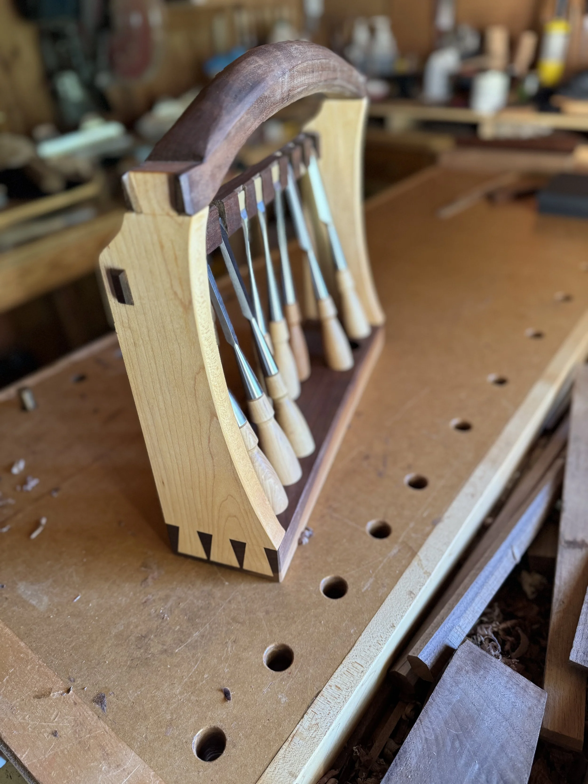 A woodworking clamp rack holding several chisels on a workbench in a woodworking shop.