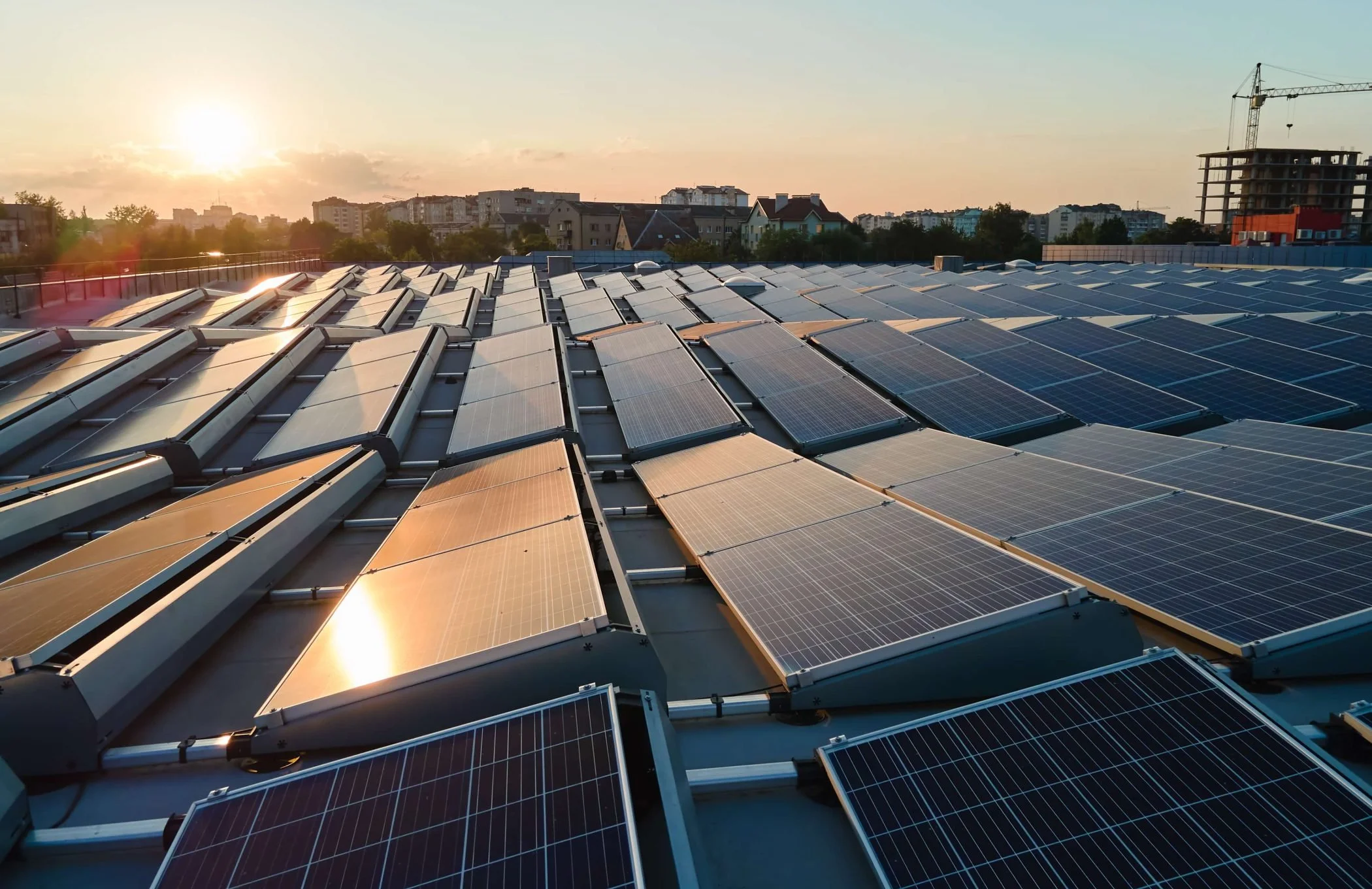 Tejado con paneles solares en un atardecer, con edificios y construcción en el fondo.