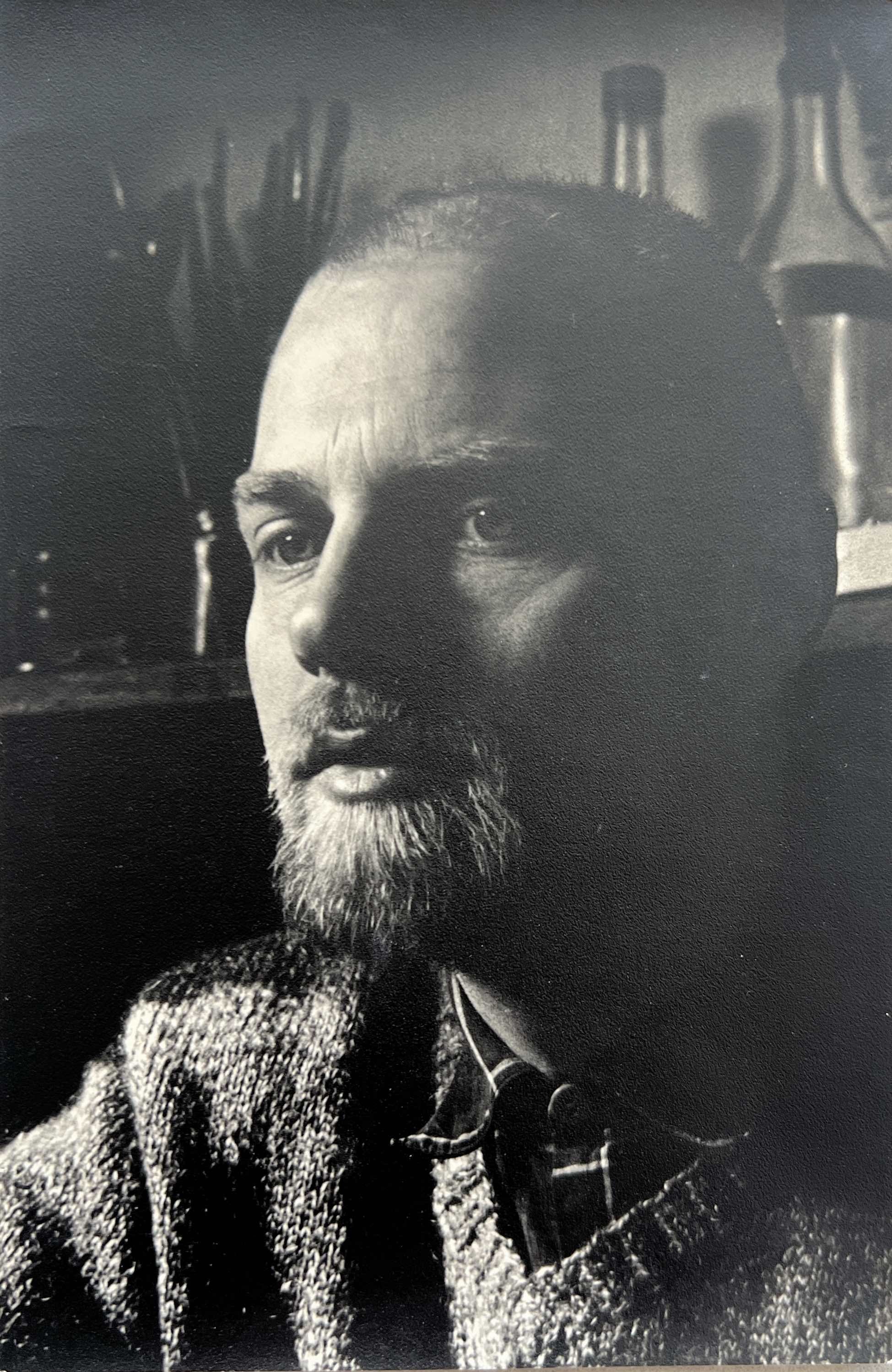 Black and white portrait of a bearded man wearing glasses, with books and a microscope in the background.